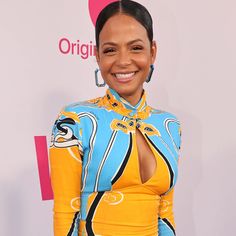 a woman in a blue and yellow dress smiles at the camera while standing on a red carpet