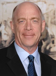 an older man in a suit and tie smiling at the camera with his eyes wide open