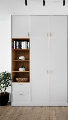 an empty room with white cupboards and bookshelves on the wall next to a potted plant