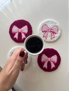 a woman holding a cup of coffee in front of three coasters with bows on them