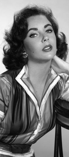 a black and white photo of a woman leaning on a stool