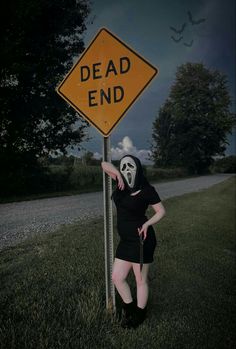 a woman wearing a mask standing next to a dead end sign