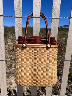 Handwoven Nantucket Lightship Basket Tote bag made by Abby Fisher. Tote features three sizes of staves in maple and cherry creating a stripe pattern on the front and back of the bag. The base and rim are made of maple and there are two Cherry inlays, one on the front of the rim and one along the top. The handles are 18” in leather to match the removable leather liner. The hydrangea charm is optional and can be purchased separately. Each piece has a logo button on the bottom of the bag with scrim Nantucket Baskets, Basket Tote, Career Fashion, 8 Weeks, Nantucket, Accessories Necklace, Old Money, Clothes Pins, Stripes Pattern