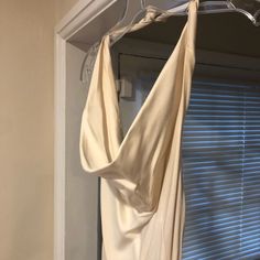 a white dress hanging on a hanger in front of a window with blind shades