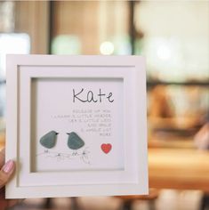 a person holding up a framed artwork with the words kate and two birds on it