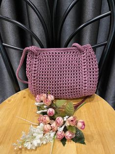 a pink crocheted purse sitting on top of a wooden table next to flowers