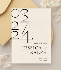 the save the date card is on top of an envelope and some flowers are next to it