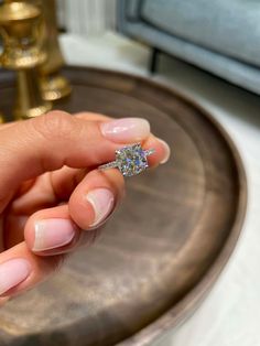 a woman's hand holding a diamond ring in front of a mirror on a table