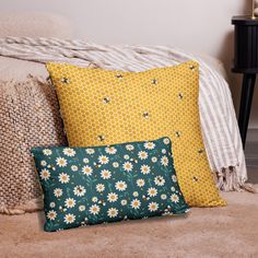 two pillows sitting on top of a bed next to a pillow with white daisies