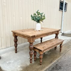 a wooden table and bench sitting in front of a building with a potted plant on top