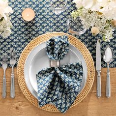 a place setting with blue and white napkins, silverware and flowers on the table