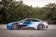 a white and blue sports car parked in a parking lot next to some trees on a cloudy day