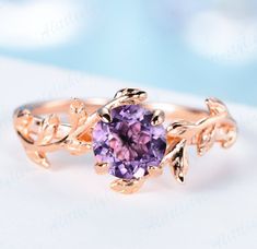 a pink ring with leaves on it and a purple stone in the center, sitting on top of a white surface