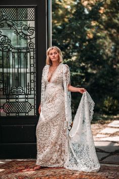 a woman standing in front of a black door wearing a white lace dress and shawl