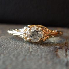 a gold and white diamond ring sitting on top of a piece of wood with an intricate design