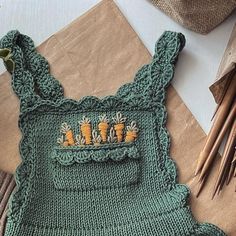 a green knitted baby romper with carrots on it