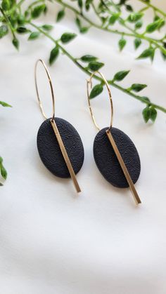 black stone earrings with gold bar detail on white surface next to green plant and leaves