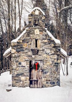 a small stone building with a red door in the middle of snow covered ground and trees behind it