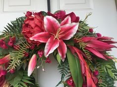 a wreath with red flowers and green leaves on the front door to a white house