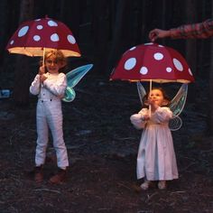 two children holding umbrellas in the woods with fairy lights on them and one child standing next to her