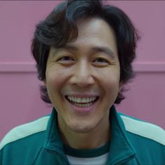 a close up of a person smiling with a pink wall in the back ground behind him