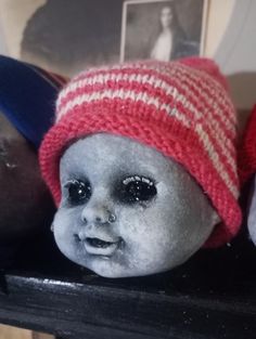 two dolls are sitting on top of a shelf with pictures in the background and one is wearing a knitted hat