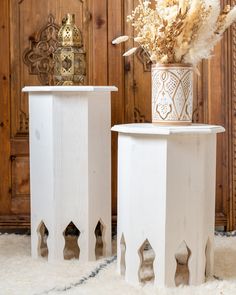 two white vases with dried flowers in them sitting on top of a rug next to a wooden door