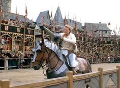 a man riding on the back of a brown horse next to a wooden fence in front of a crowd