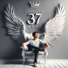 a man sitting on top of a white chair in front of a wall with angel wings