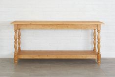 a wooden table sitting on top of a floor next to a white brick wall in an empty room