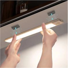 two hands are holding the lights on top of a light fixture in front of a mirror