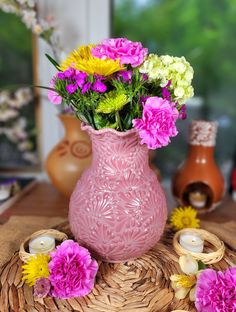 a pink vase filled with lots of flowers on top of a wooden table next to candles