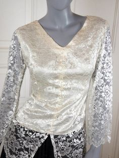 This stunning Hungarian vintage lace blouse was custom made in 1992 and has been stored lovingly since then, and so it is in near mint condition. The lace top has a V neckline and long bell-shape sleeves with scalloped cuff edging. The bodice is fully lined to the hip in ivory polyester. The floral lace continues for a further 7 inches (17.78cm) below the waistline and has a scalloped hemline. Five pearl decorative buttons feature on the front of the bodice, and a side zipper makes it easy to sl Vintage Lace Top, Vintage Lace Blouses, Top With Bell Sleeves, Vintage Clothes Women, White Lace Top, Decorative Buttons, Beautiful Blouses, Elegant Floral, Blouse Length