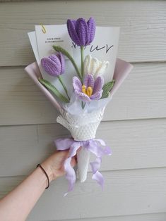 a hand holding a bouquet of crocheted flowers on top of a white wall