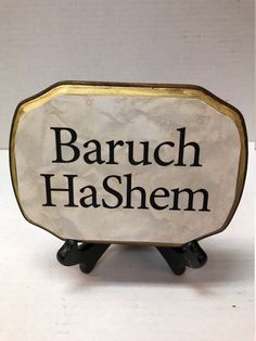 a sign that says baruch hashem on it's stand in front of a white wall