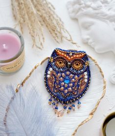 a beaded owl sitting on top of a white plate next to a candle and some feathers