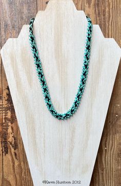 a blue beaded necklace sitting on top of a piece of wooden plank next to a white mannequin