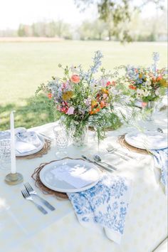 the table is set with plates, silverware and flowers in vases on it