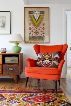 an orange chair sitting in front of a painting on the wall next to a lamp