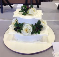 a three tiered cake with white roses and green leaves on the top is sitting on a table