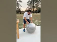 a man is doing something on top of a large metal ball in the grass outside