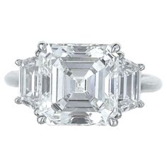 This exquisite ring showcases a captivating 4.19-carat square emerald-cut diamond, certified by GIA, known for its precision and craftsmanship. The center diamond, beautifully complemented by trapezoid side stones, exudes an understated elegance. With a color grade of H, the diamond exhibits a subtle warmth while maintaining exceptional brilliance. Its VS1 clarity grade ensures that inclusions are minimal and not visible to the naked eye, allowing the diamond to maintain its clean and radiant ap Unique Diamond Wedding Rings, Asscher Cut Diamond Ring, Asscher Cut Engagement Rings, Emerald Cut Diamond Ring, Wedding Ring For Her, Asscher Cut Diamond, Engagement Ring Diamond Cut, Detailed Jewelry, Emerald Cut Diamond