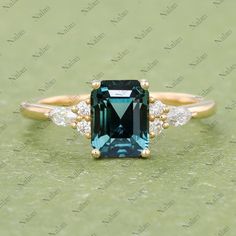 an emerald and diamond ring with two diamonds on the side, sitting on a green surface