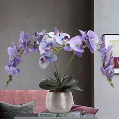 purple flowers are in a white vase on a table next to a pink couch and pillows