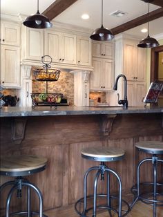 a kitchen with three stools in front of an island and two lights hanging from the ceiling