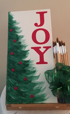 a wooden box with paint and pencils in it next to a christmas card that says joy