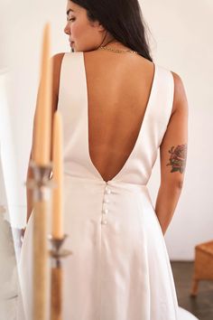 a woman in a white dress standing next to candles and looking at the back of her dress