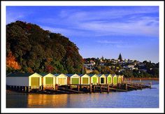 a row of beach huts sitting on top of a lake next to a forest covered hillside