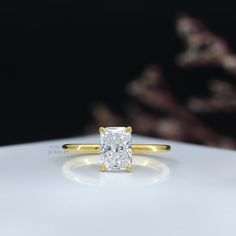 a yellow gold engagement ring with a princess cut diamond in the center on a white surface