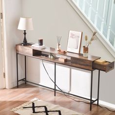 a wooden table sitting under a stair case next to a lamp on top of a hard wood floor